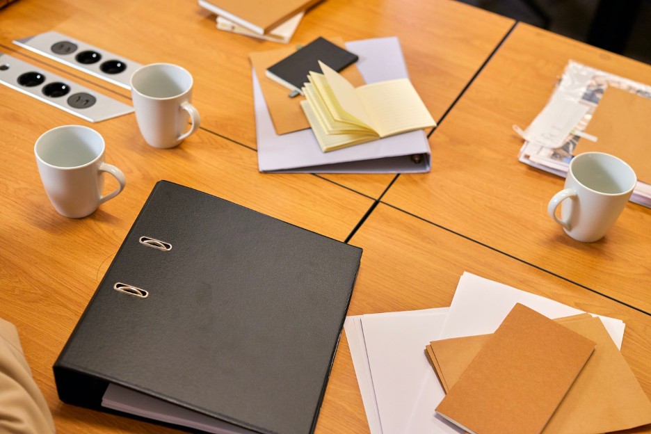 A table with folders, files, and other documents and mugs.